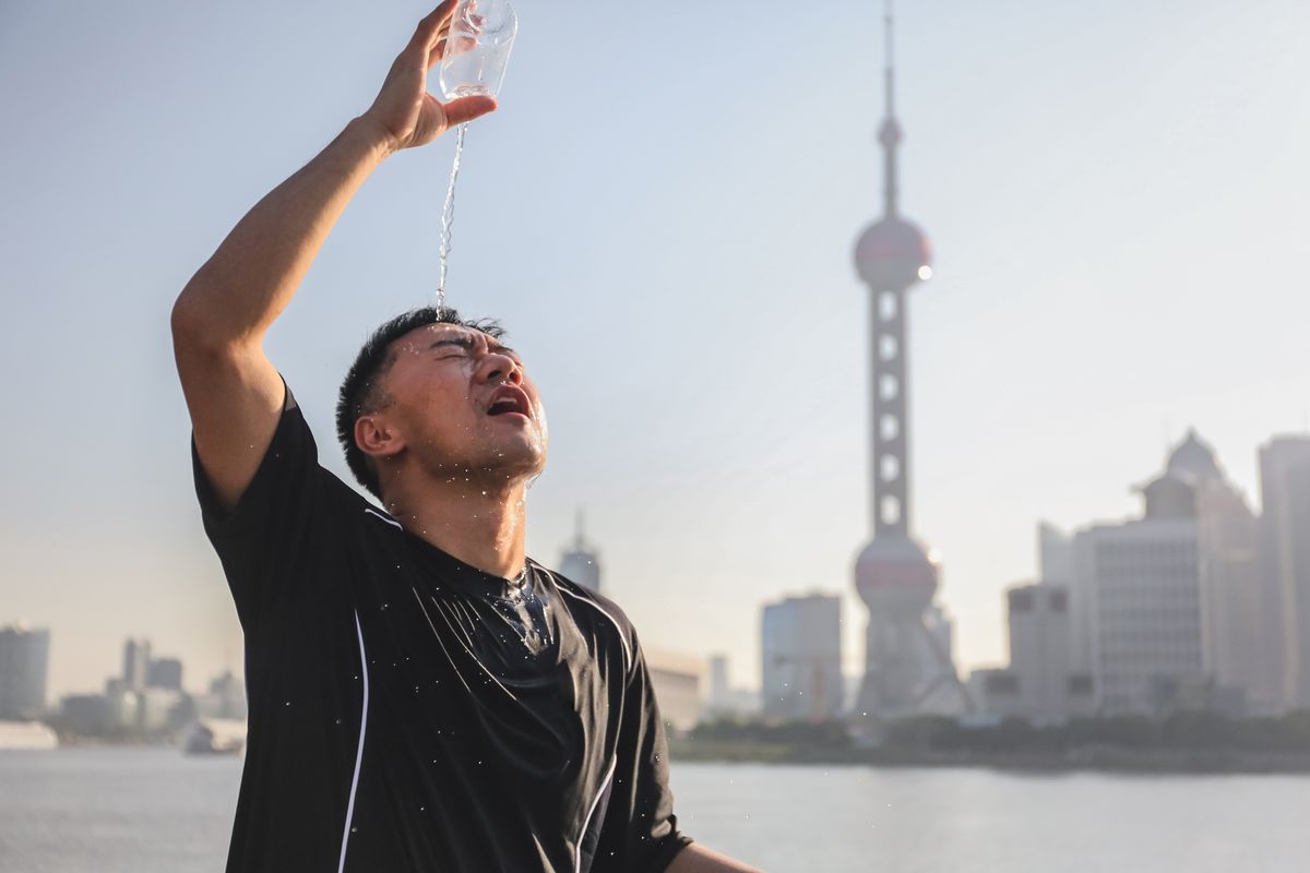 runner pouring water over his head with famous skyline of lujiazui financial district, the bund, shanghai