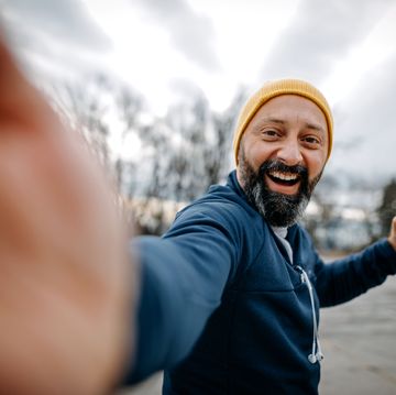 happy mature man with knit hat taking a selfie and holding water bottle and resistance band during jogging outdoors