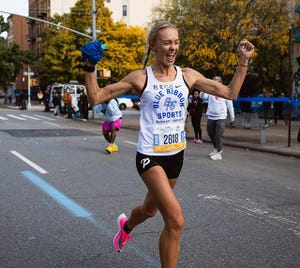 una atleta corriendo una maratón en mitad de una ciudad y con los brazos en alto