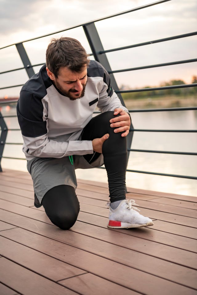 sportsman has pain in his knee during a relaxation exercise near the river bank handsome young athlete in sports suit is having a knee injury during morning running in the city