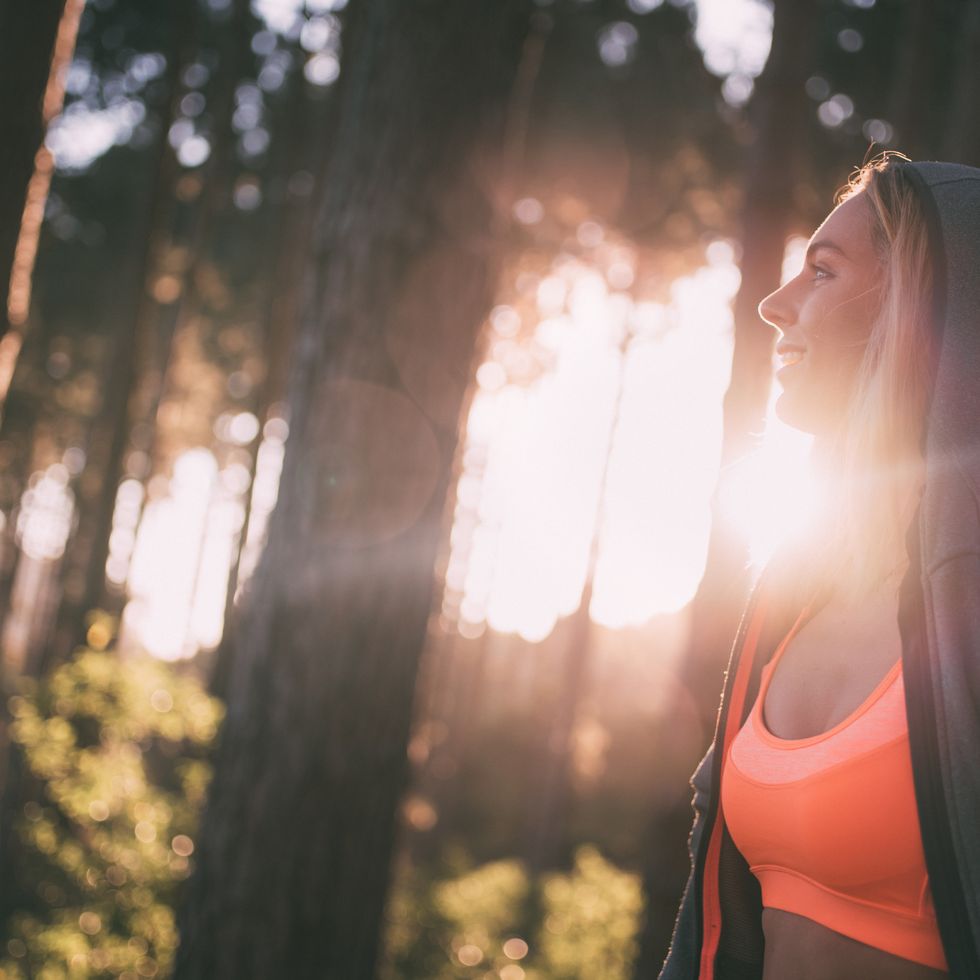 Runner smiling at a beautiful forest view with morning sunflare