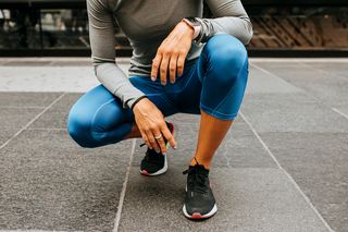 runner in leggings squatting on sidewalk