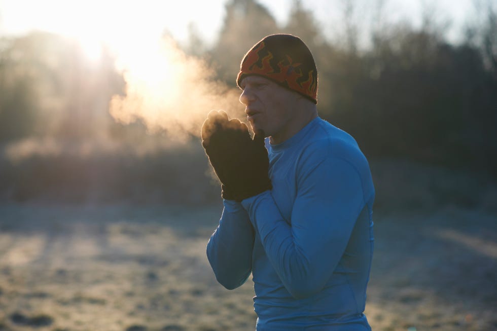 runner wearing knit hat and gloves, rubbing hands together, breathing cold air