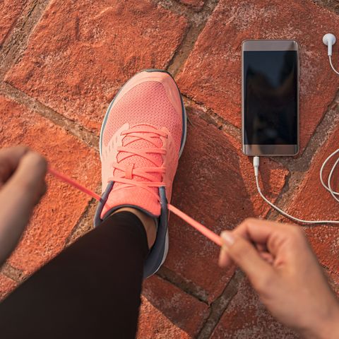 runner woman tying running shoes laces getting ready for race on run track with smartphone and earphones for music listening on mobile phone athlete preparing for cardio training feet on ground