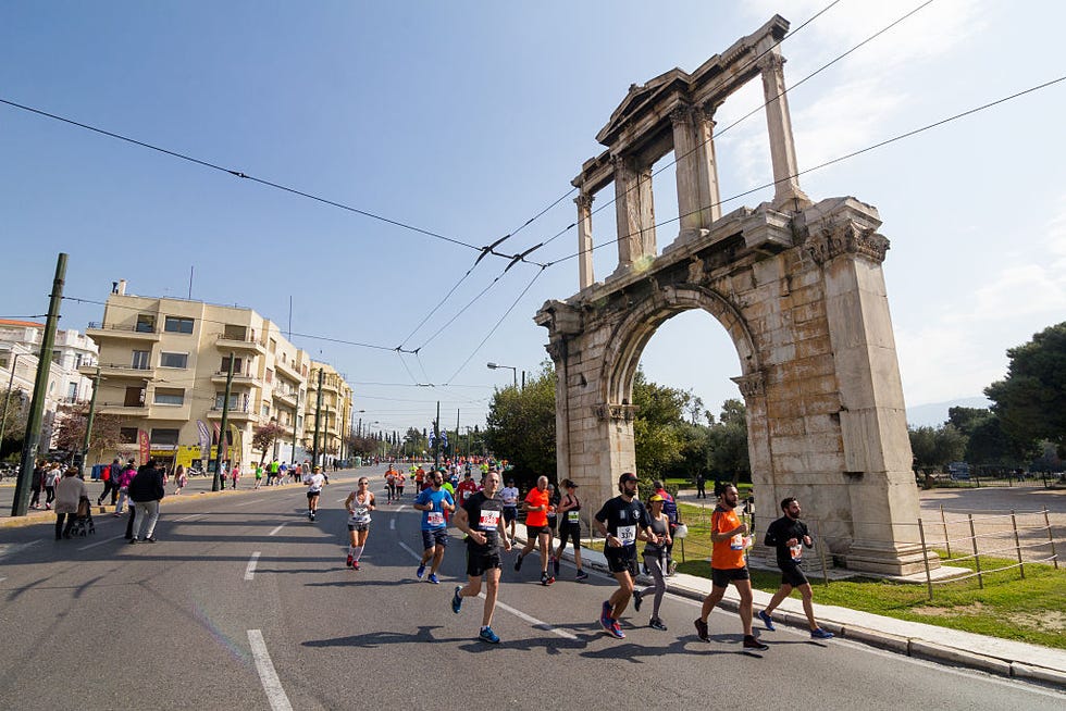 a group of runners in a race pass in front of an ancient ruin in athens