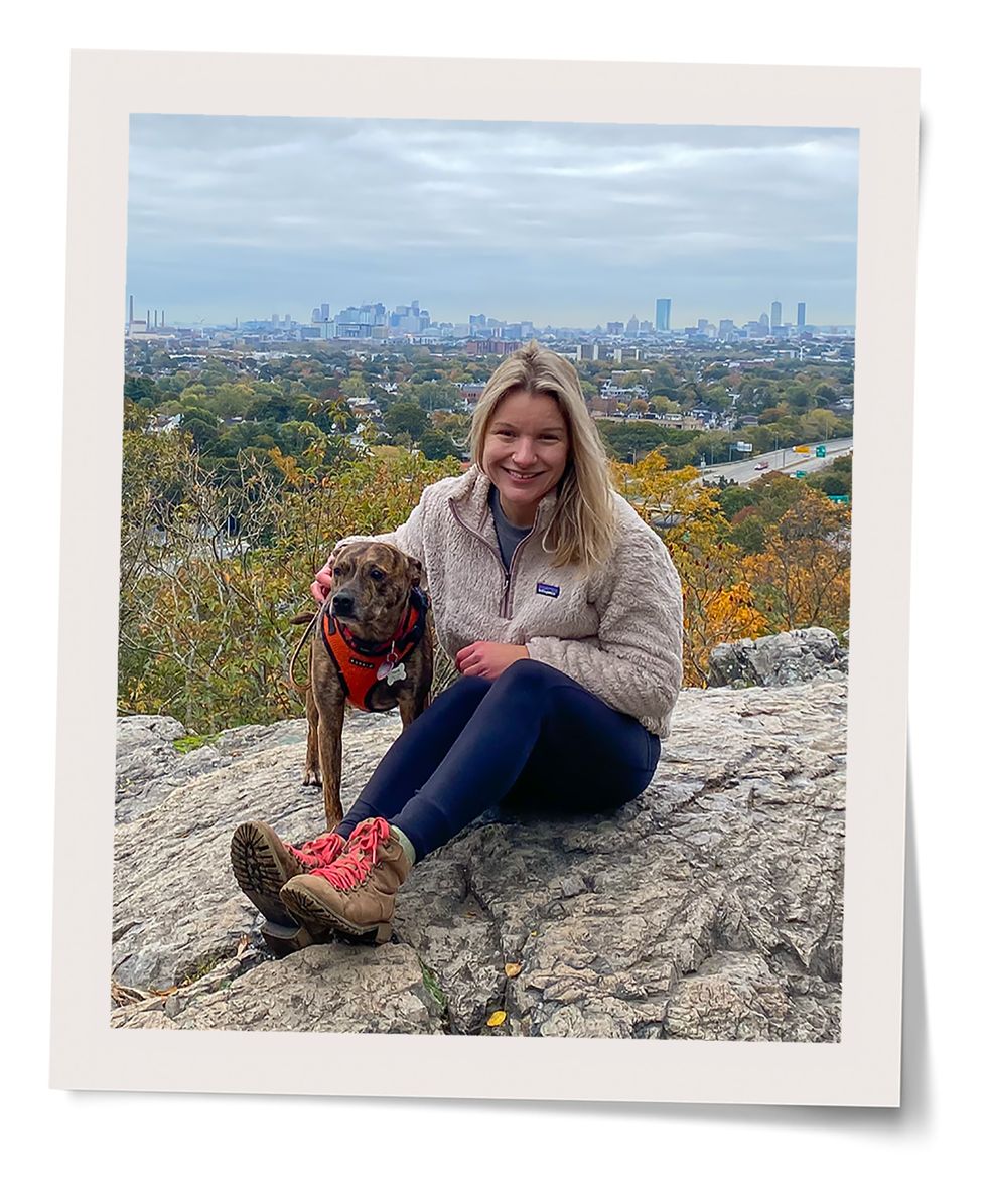 dog and woman sitting on rock with city in background