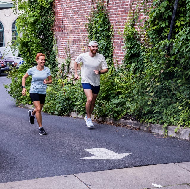 two runners run past a brick building covered in ivy