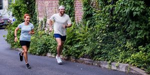 two runners run past a brick building covered in ivy