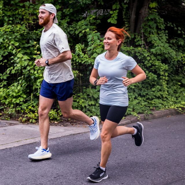 a man and woman jogging past a wall covered in ivy