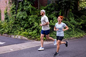 a man and woman jogging past a wall covered in ivy