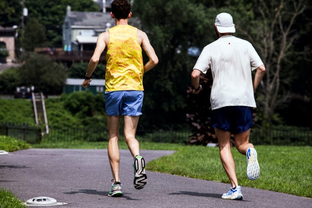 two runners jogging on a path surrounded by greenery and buildings in the background