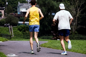 two runners jogging on a path surrounded by greenery and buildings in the background