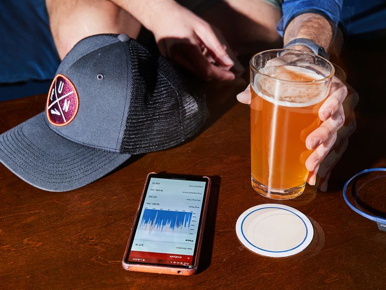 running Paris hat, fitness tracker app, headphones and glass of beer on coffee table