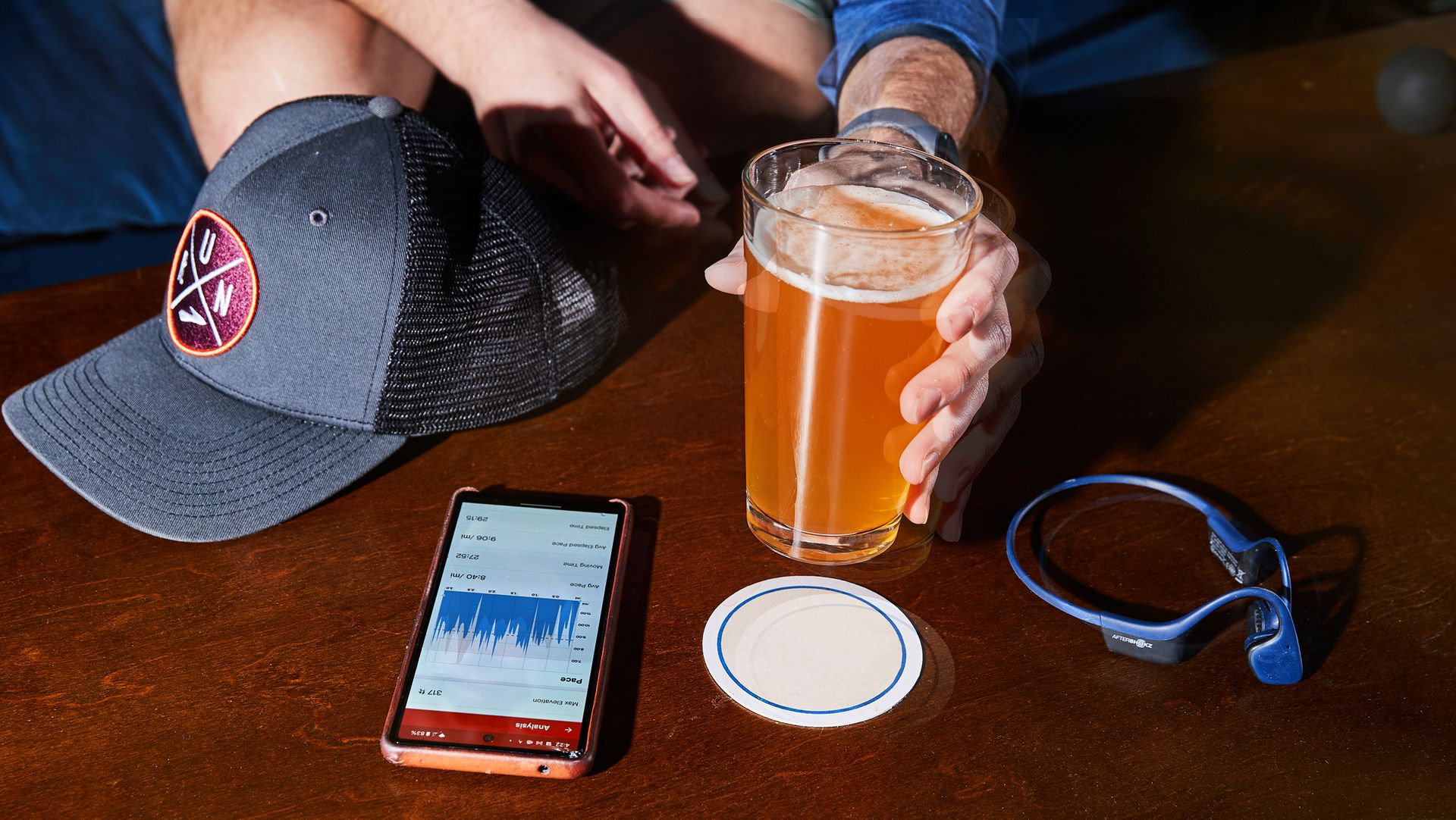 running hat, fitness tracker app, headphones and glass of beer on coffee table