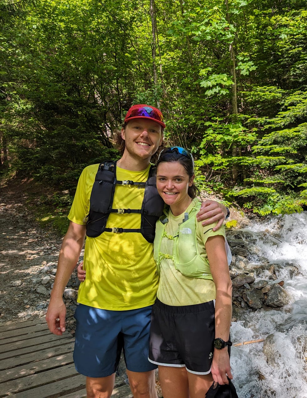 man and woman pose for a picture by a waterfall while running the mountains