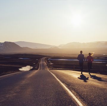 running couple on road towards sunlit mountains