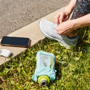 runner lacing up shoes with water bottle, airpods, phone and sunglasses on curb