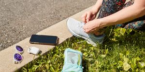 runner lacing up shoes with water bottle, airpods, phone and sunglasses on curb