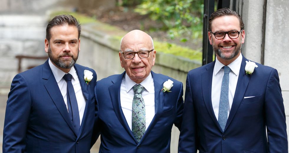 lachlan murdoch, rupert murdoph, and james murdoch pose for a photo while standing outside, the men wear matching navy suits with white shirts and various blue ties, each has a white rose on his lapel