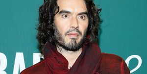 russell brand poses in a red top against a turquoise background at an event for his book launch