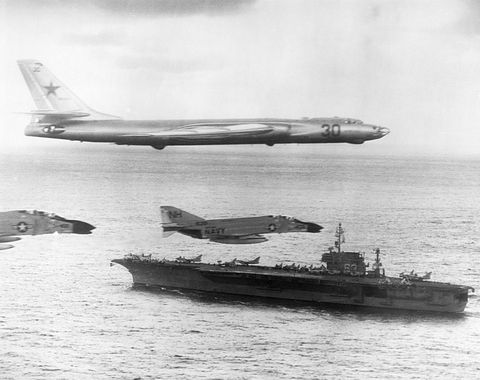 tupolev tu16 bomber flying with navy escort over aircraft carrier