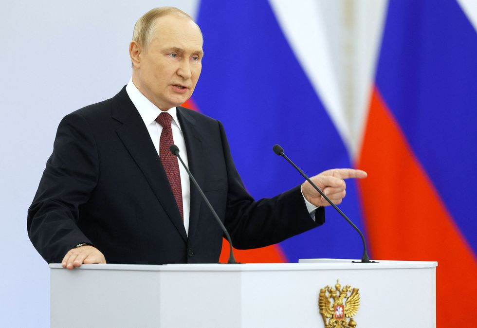 vladimir putin pointing with his left hand as he speaks at a podium