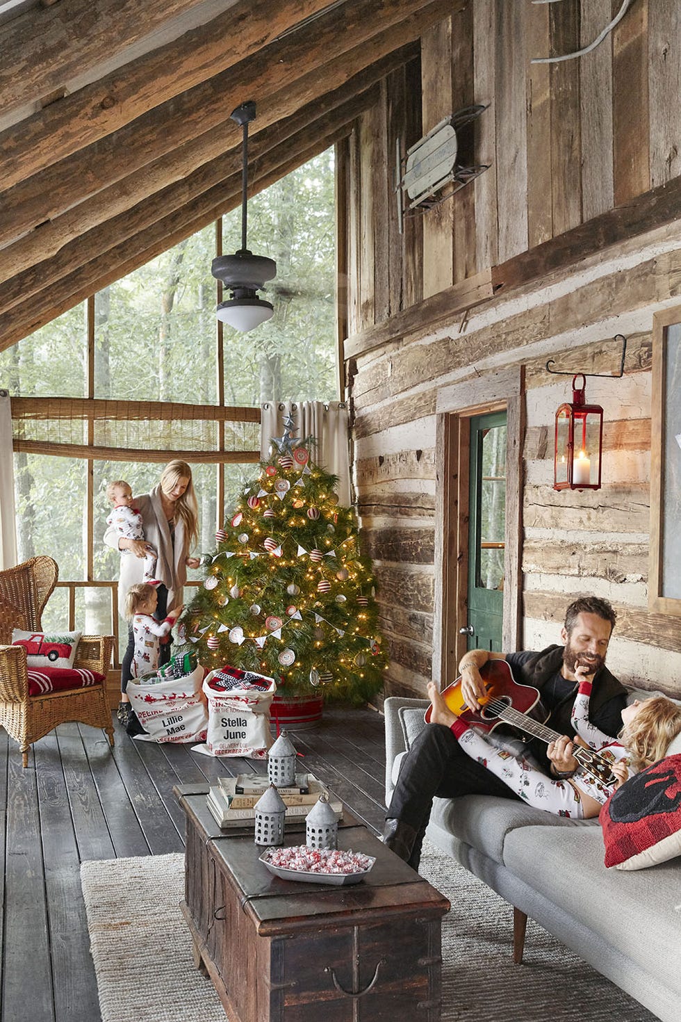 cabin porch with tree in a galvanized tree skirt with red stripe, family hanging around the tree and on the nearby sofa playing guitar