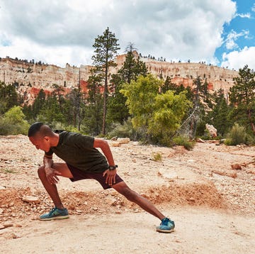 a man stretching on a dirt trail with trees and a mountain in the background a man stretching on a dirt trail with trees and a mountain in the background