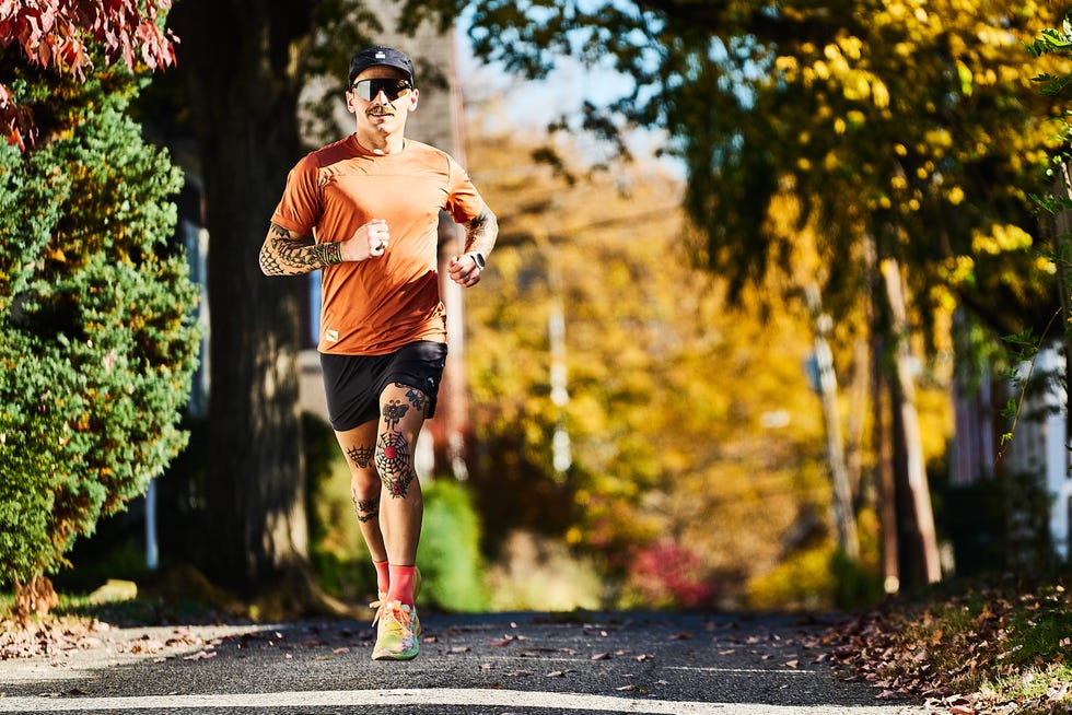 A runner in an orange shirt and shorts on a treelined path during autumn