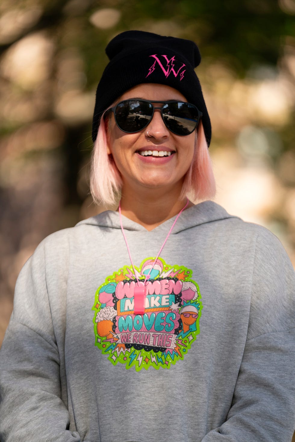 a woman with pink hair and a sweatshirt reading women make moves we run this poses for a portrait