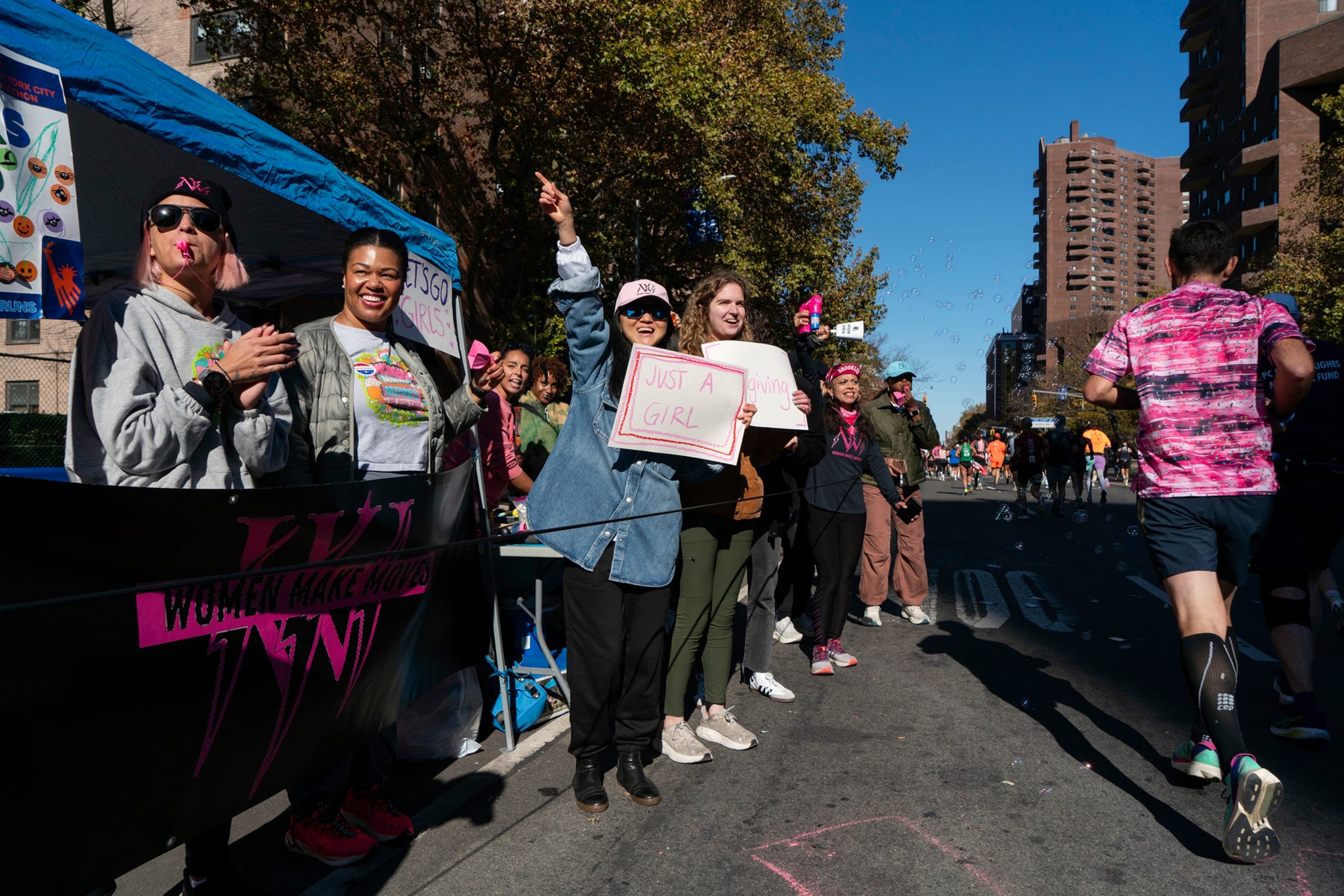 people holding signs cheer for runners at the side of a street