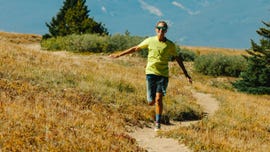 Individual running along a winding dirt path in a grassy area with trees in the background