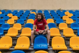 a man wearing running clothing sits in a stadium with yellow and blue chairs