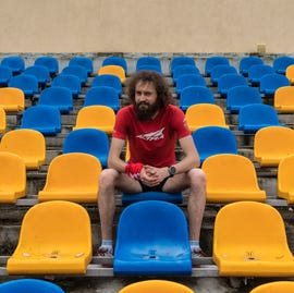 a man wearing running clothing sits in a stadium with yellow and blue chairs a man wearing running clothing sits in a stadium with yellow and blue chairs