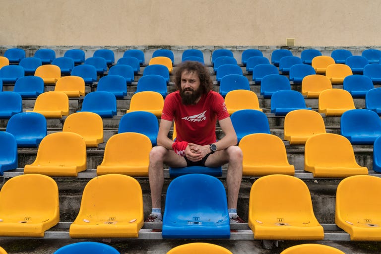 a man wearing running clothing sits in a stadium with yellow and blue chairs