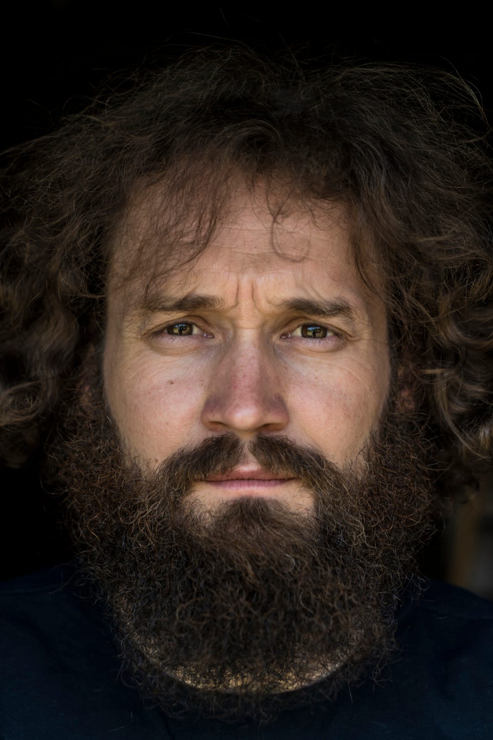 a bearded man with long hair poses for a portrait against a black background