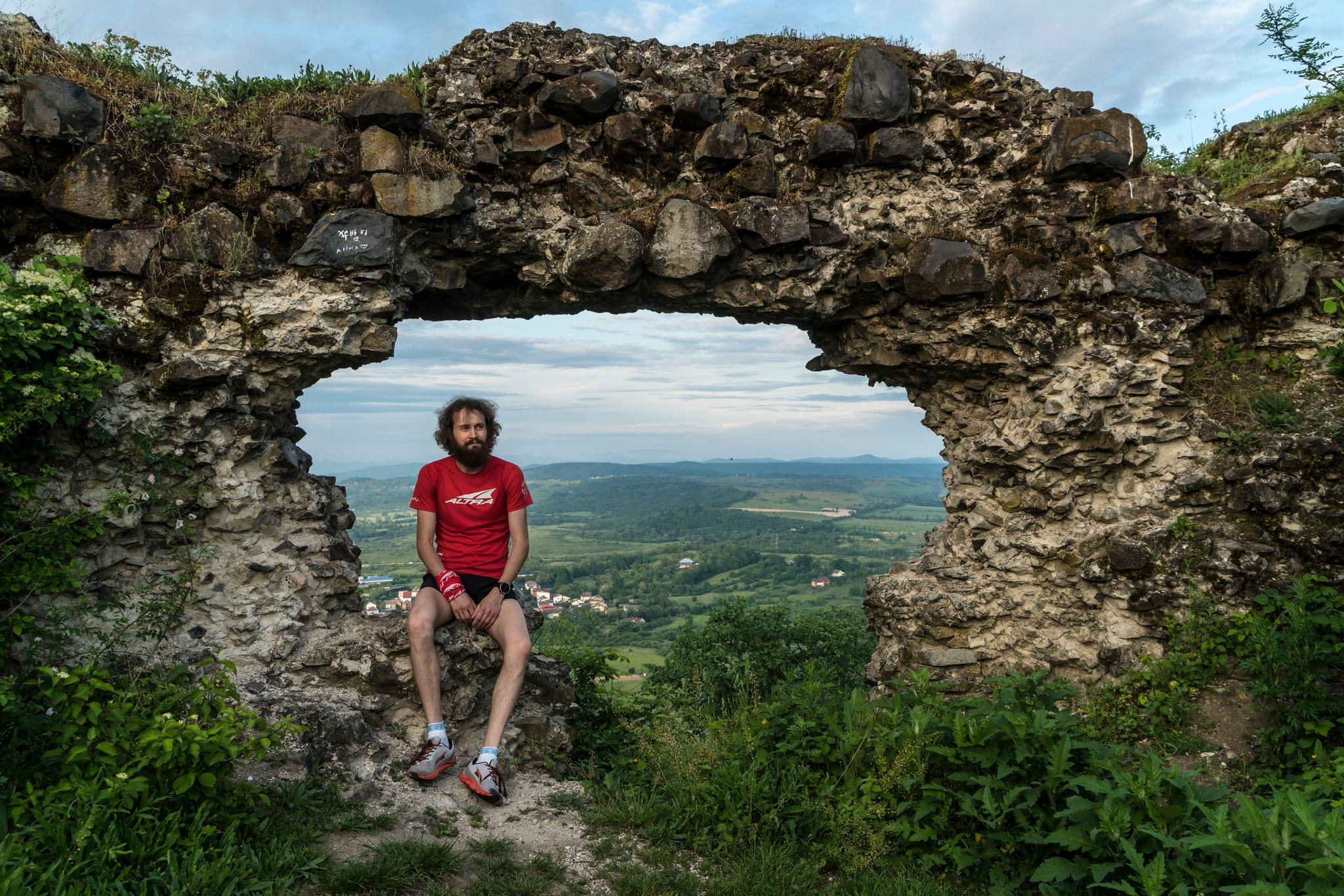 a man wearing running clothing sits on a rock on a hill with ruins