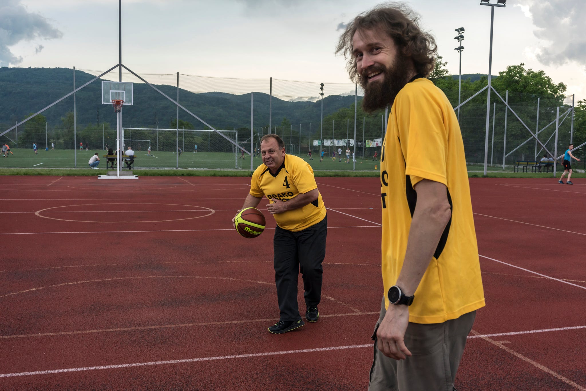 two men wearing matching yellow shirts playing basketball