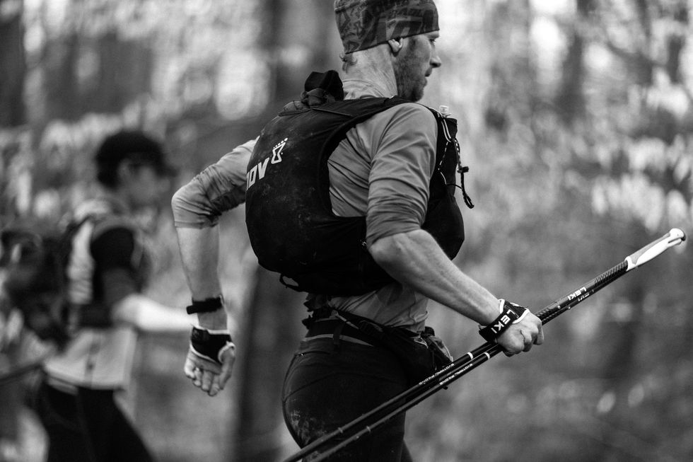a trail runner holds his trekking poles in his hand as he runs