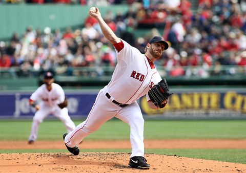 red sox pitcher ryan dempster throws a pitch from the mound, behind him is a blurry teammate and part of the crowd