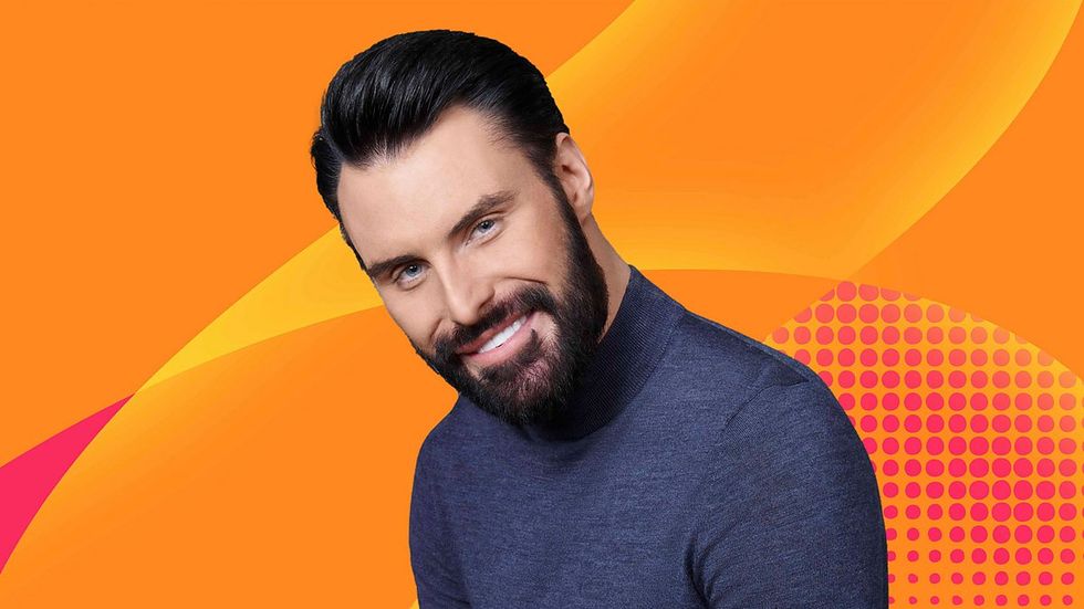 Werbebild von Rylan BBC Radio 2, lächelnd in einem blauen Rollkragenpullover vor einem orangefarbenen Hintergrund