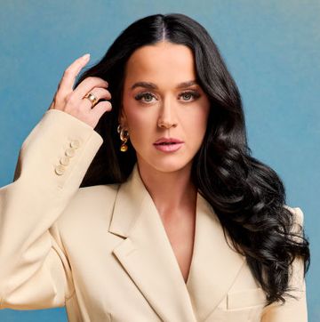 katy perry poses in a cream suit with her long hair down against a blue and yellow fade background