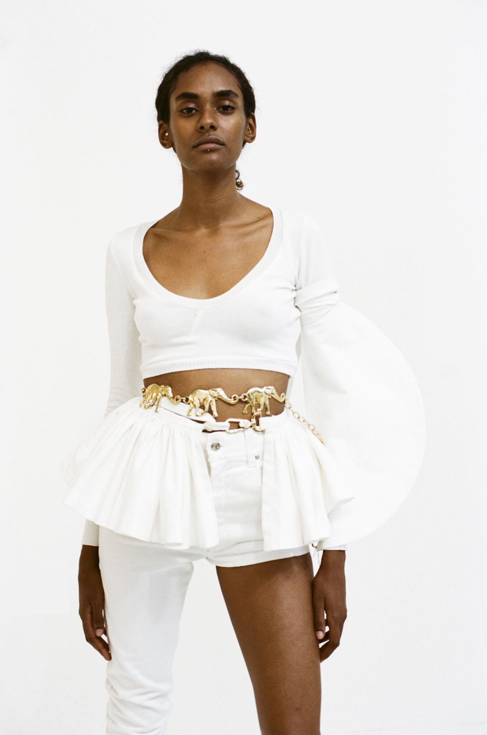 a model wearing a custom pair of one leg flare pants, and a pleated skirt belt accessory both by designer sarah aphrodite