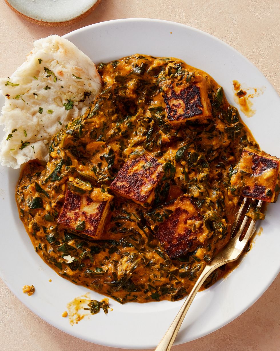 white bowl of saag paneer with a gold fork and a torn piece of naan