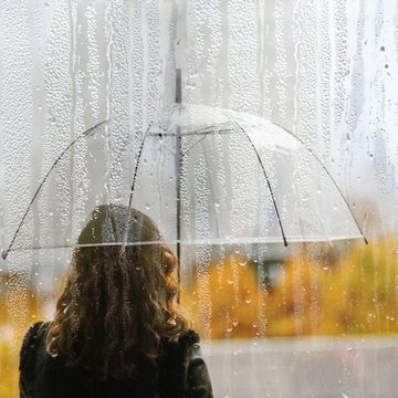 a woman silhouette with transparent umbrella through wet window with drops of rain during autumn