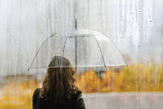 a woman silhouette with transparent umbrella through wet window with drops of rain during autumn