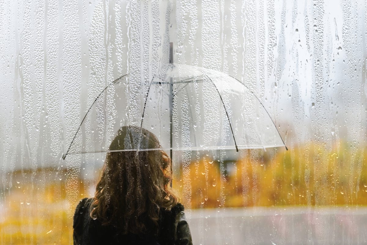 a woman silhouette with transparent umbrella through wet window with drops of rain during autumn