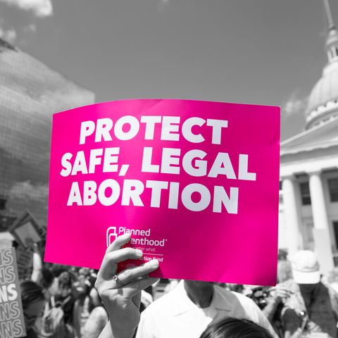 woman holding sign that reads "protect safe, legal abortion"