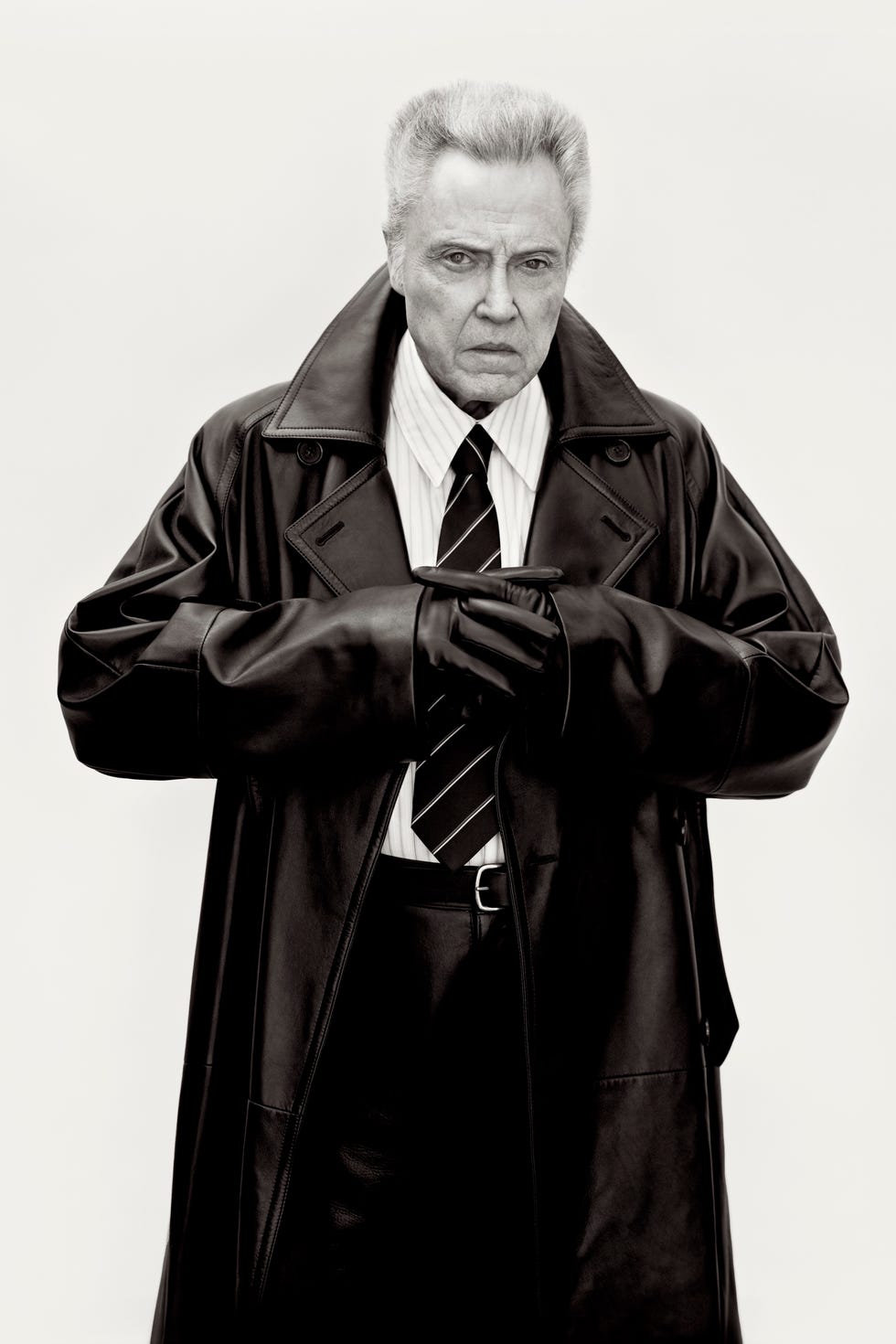 a man dressed in a black trench coat and formal attire arms crossed