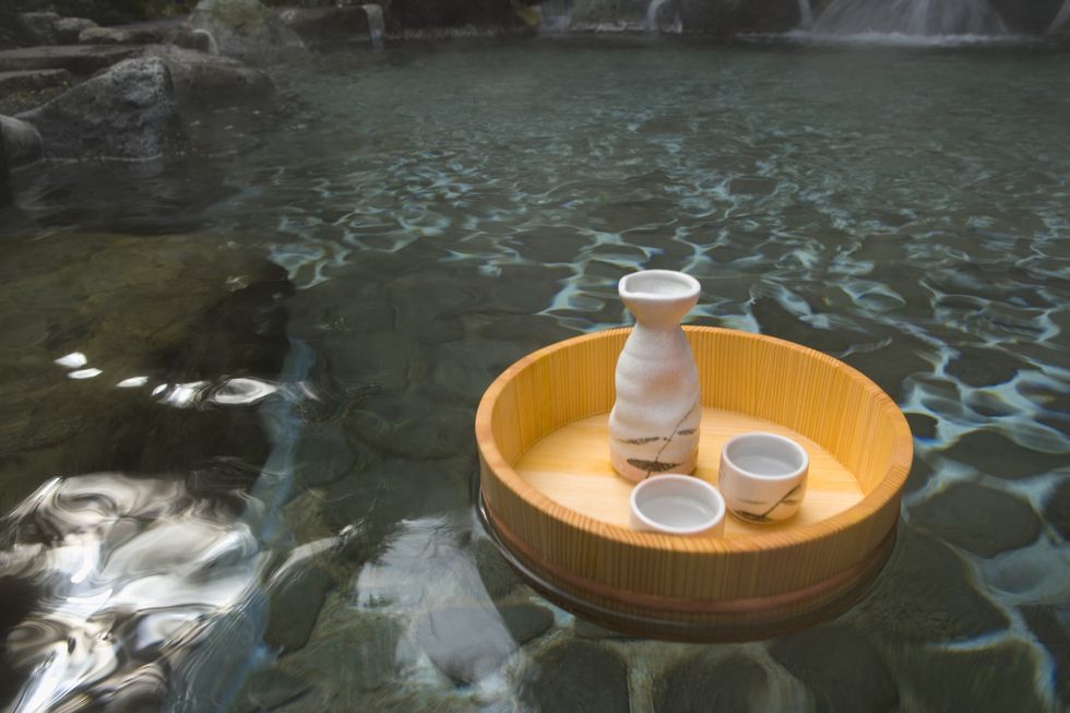 sake bottle and cups in a wooden tub floating on a japanese public bath, hot spring, high angle view, japan